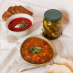 Zwei Teller Suppe mit Gewürzgurken, Brott und einem Strauß Trockenkräuter
